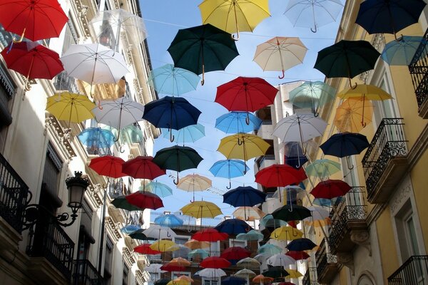 Bunte Regenschirme hängen über der Straße zwischen Gebäuden vor einem blauen Himmelshintergrund