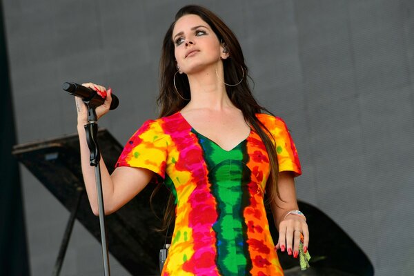A dark-haired singer in a bright dress on stage with a microphone in her hand