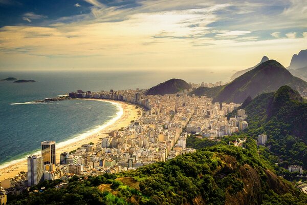 A long sandy beach on the coast with tall buildings and mountains