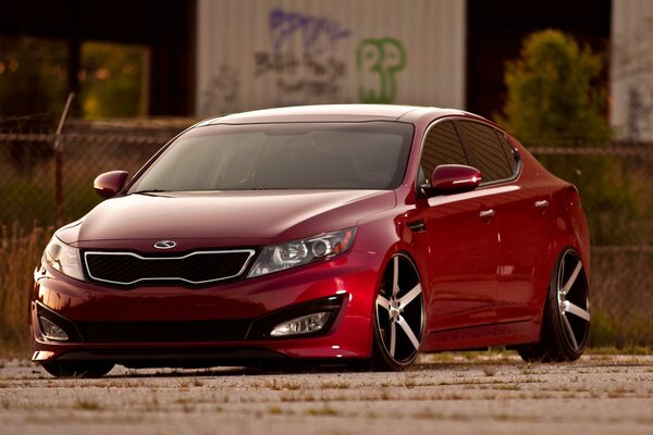 A red kia car standing on the sidewalk against the background of graffiti-painted garages