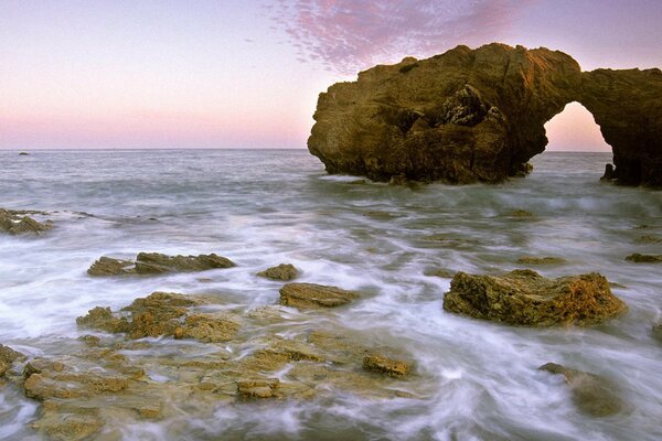 A rocky beach lights up a pink sunset