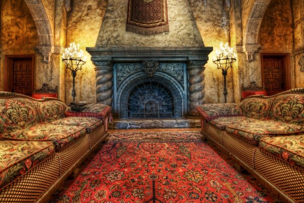 Inside the house there is a fireplace on the sides there are large candlesticks with burning candles, doors on both sides, sofas with patterns between them a carpet with a red color