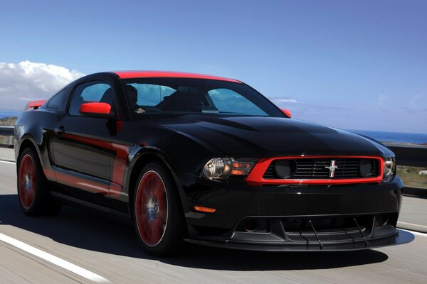 A black car with a red frame is driving on the road against a blue sky background