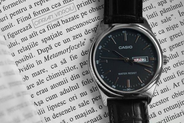 A watch with a black dial is lying on a book