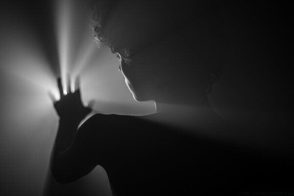 A silhouette of a man covering a light source with his hand