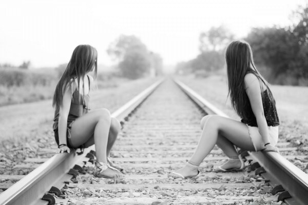 Two girls are sitting on the railway tracks