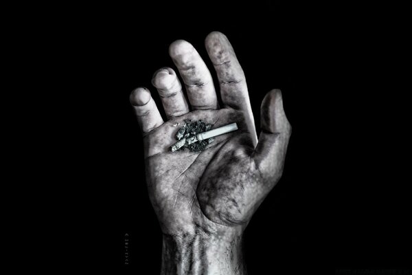 A hand and a decayed cigarette on a black background