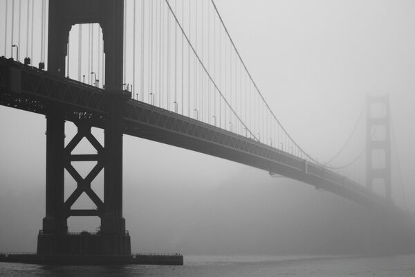 Foto en blanco y negro de un puente colgante en la niebla