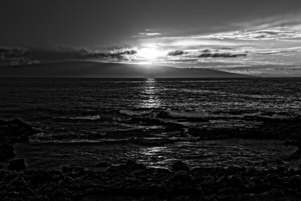 Black and white photo of sea water from the beach against the sunset background