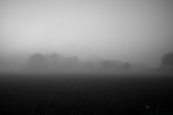 Schwarz-Weiß-Foto eines Feldes von Dorfhäusern im Nebel