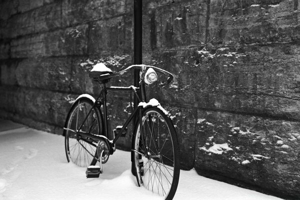 A snow-covered bicycle by a stone wall