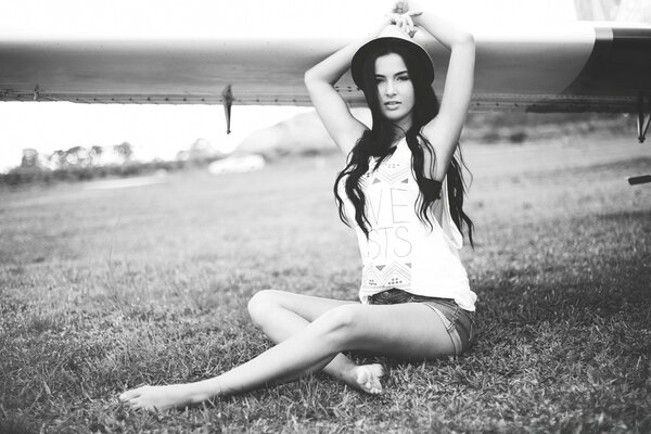 The brunette is sitting by the pond in a model hat