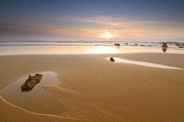 Praia de areia com pedras ao pôr do sol