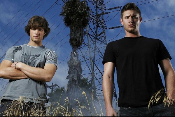 Two actors from the TV series Supernatural in a field against the background of power lines.