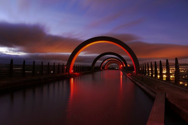 Sonnenuntergang am Himmel hinter der Brücke vor dem Hintergrund des Wassers in einer anderen Stadt