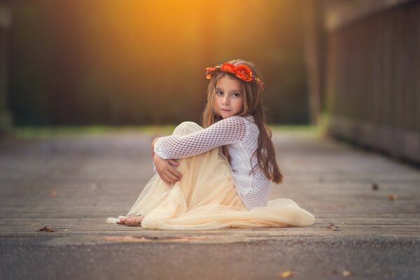 Petite fille sur le sol avec une Couronne de fleurs rouges