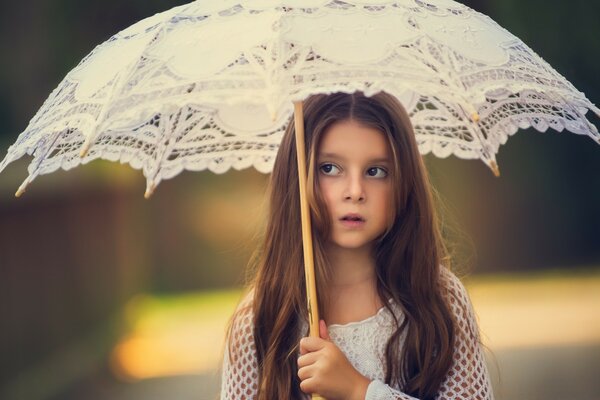 A little girl with a white umbrella and a blurry background