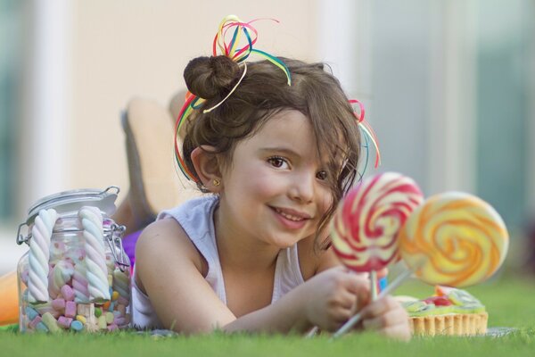 Una niña sonriente yace en la hierba y sostiene dulces en sus manos