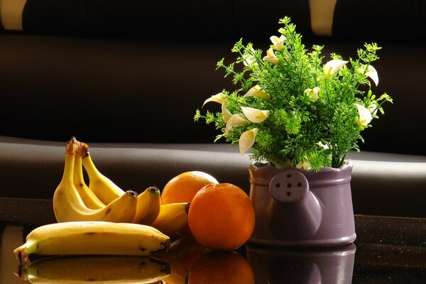 Obok bukietu kwiatów leżą banany i pomarańcze