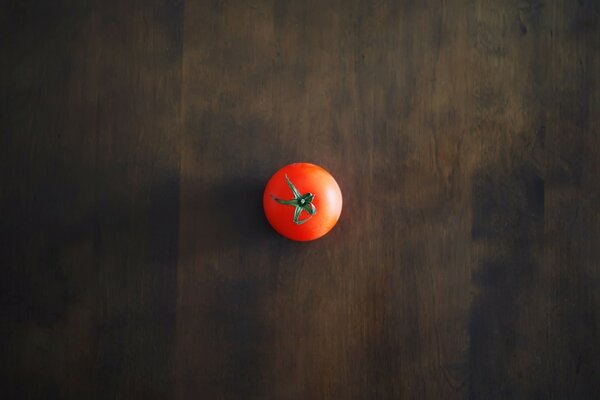 Eine rote Tomate liegt auf einem dunklen Holzboden