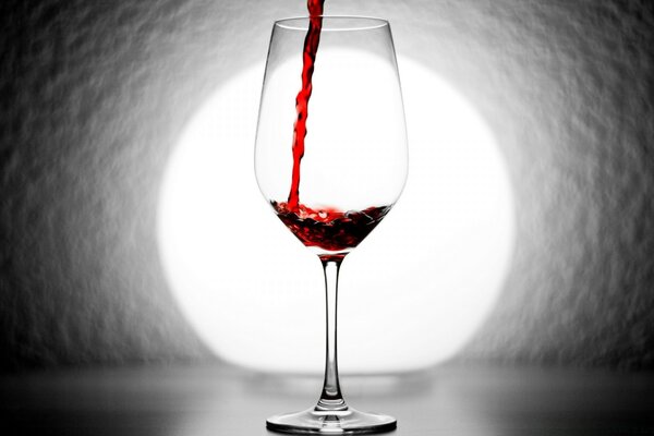 Pouring red wine with a transparent glass on a background of light