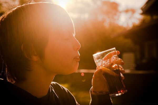 Enfant avec les yeux fermés de plaisir . boire une boisson dans un verre