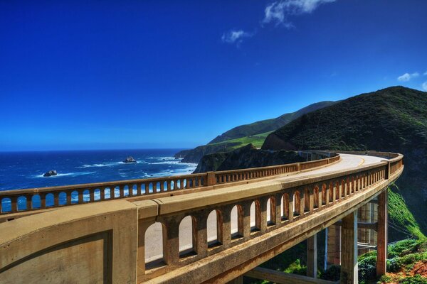 A bridge over the blue ocean leading to the hills