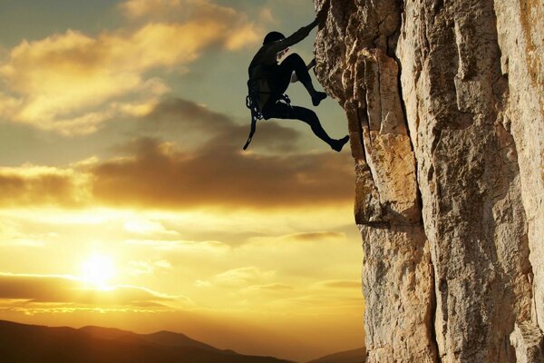 Escalador en una roca escarpada en el fondo de la puesta de sol