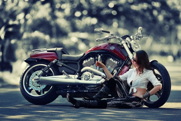 A girl is sitting by a red motorcycle