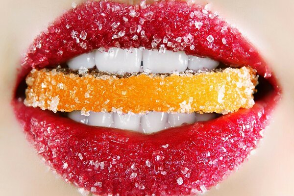 Weibliche Lippen halten eine Scheibe Zuckerfrucht