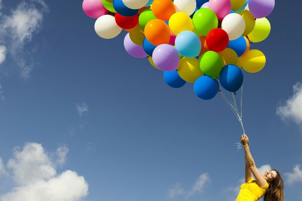 A girl holds colorful balloons against the sky background