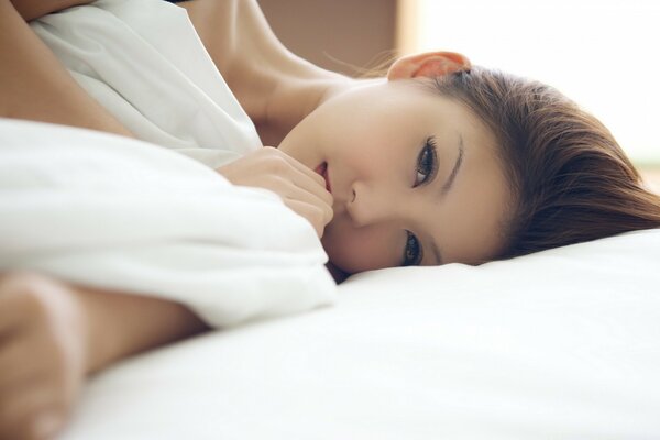 Asian girl on snow-white bed linen