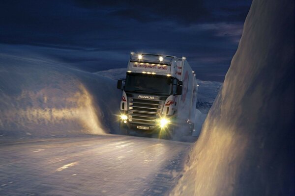 Ein Lastwagen, der auf einer schneebedeckten nächtlichen Wintertrasse bergauf fährt