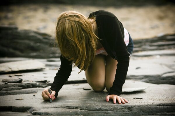 A young girl draws on a stone