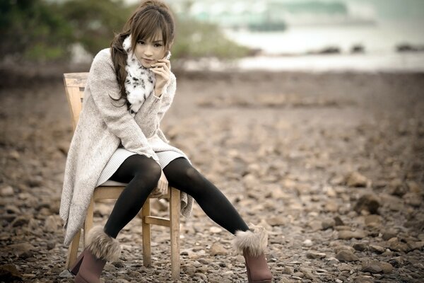 A girl is sitting on a chair near the ocean