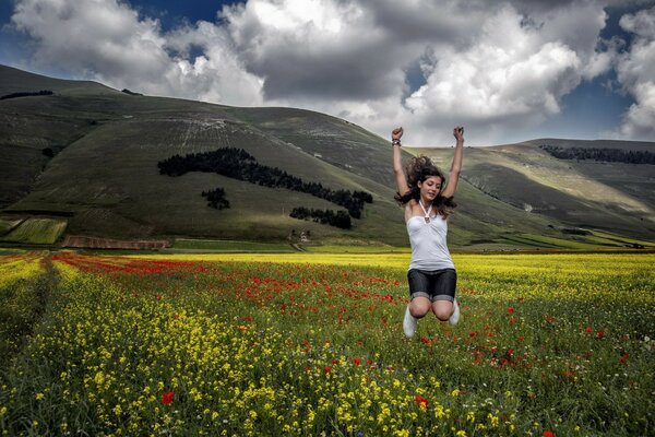 Paesaggio con una ragazza che salta in un campo sullo sfondo delle montagne