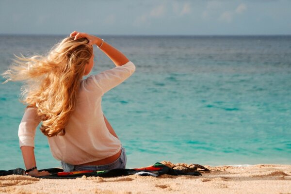 A girl with long hair is sitting on the seashore