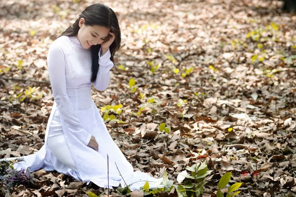 La chica de blanco se sienta en las hojas de otoño