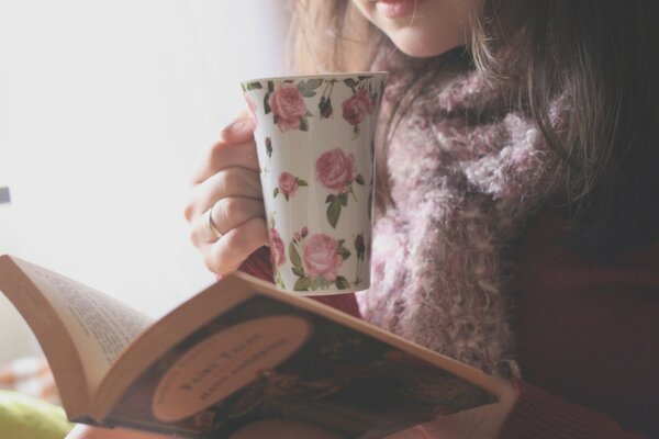 A girl is reading a book and drinking tea