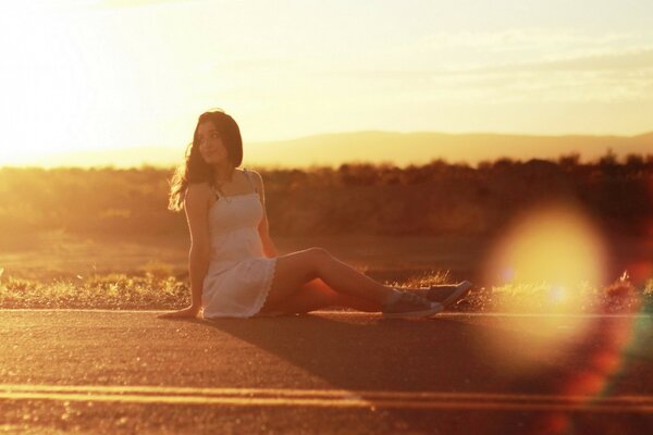 Chica sentada en la carretera en el fondo de la puesta de sol