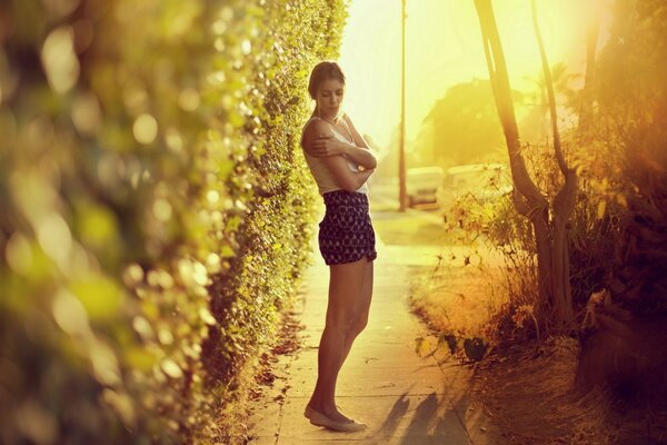 Mädchen in Shorts und Ballerinas umarmt sich mit ihren Händen vor dem Hintergrund eines Gartenweges