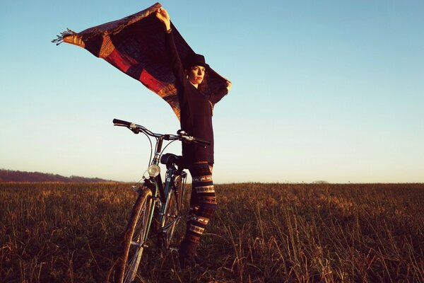 A girl with a bicycle holds a handkerchief over her head in the wind