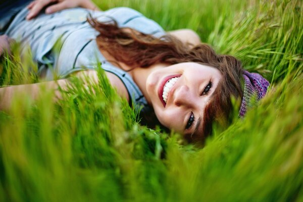 Una chica con el pelo largo se acuesta y sonríe en la hierba verde