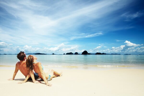 A guy and a girl on the beach next to the sea look at the blue sky