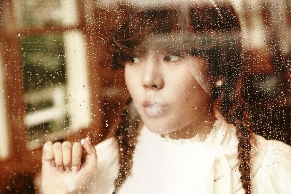 The girl looks through the wet glass