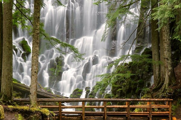 Wooden beam bridge on the background of a waterfall