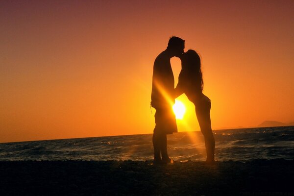 Pareja besándose en el fondo de la puesta de sol junto al mar