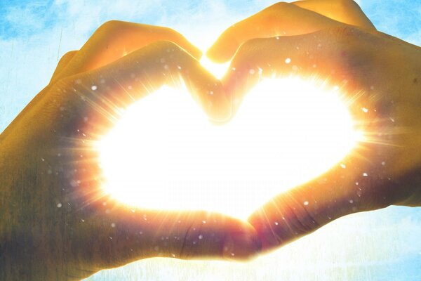 Hands folded with a heart, through which the rays of the sun penetrate