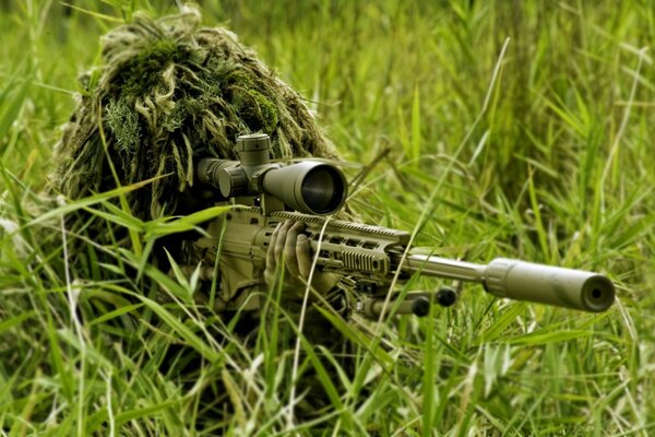 A sniper with a rifle in the grass takes aim