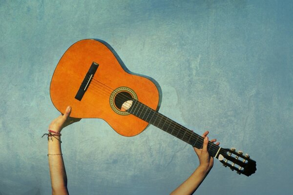 Guitar in the hands of a man over his head on a blue background